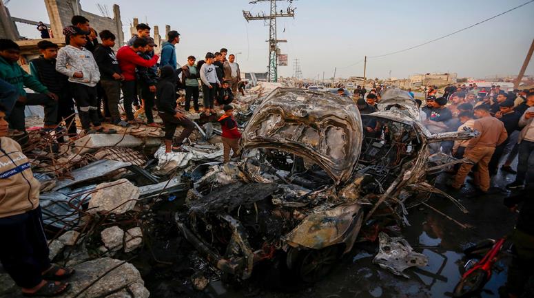 مواطنون يتفقدون مركبة على شارع صلاح الدين قرب مدخل مخيم المغازي استهدفها الاحتلال ما أسفر عن استشهاد شخص وإصابة آخرين